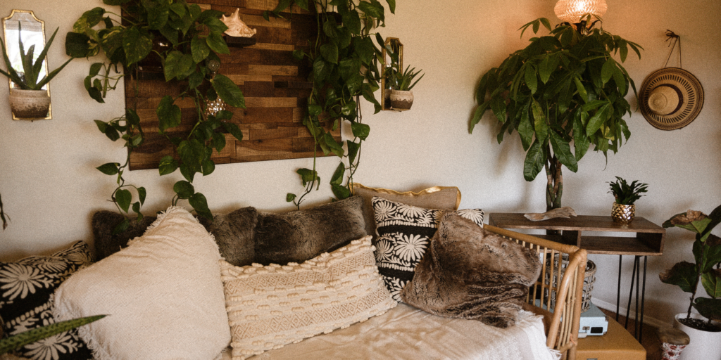 a hygge interior of a room featuring plants, throw pillows, wallboard and cushions