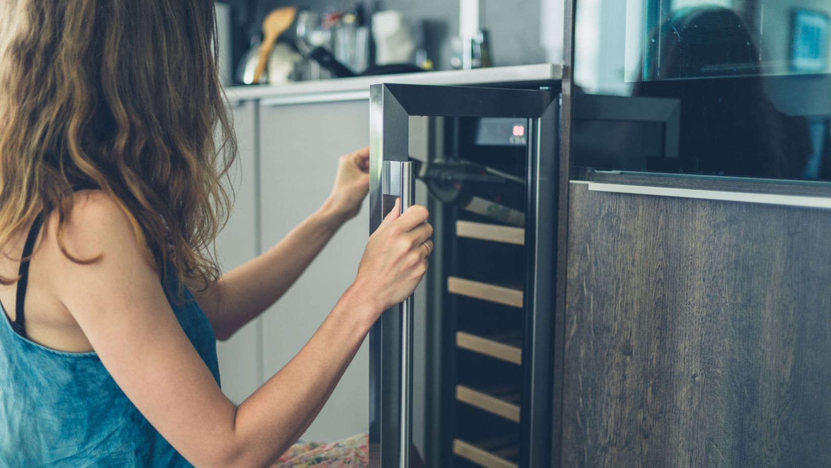 A woman reaching into a wine cooler