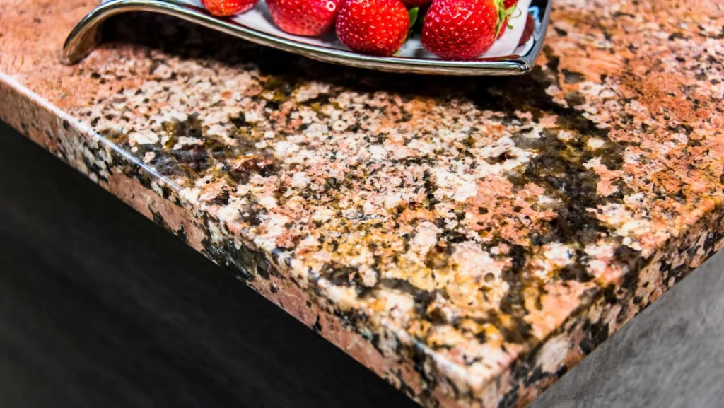 A granite kitchen countertop with a bowl of strawberries on top